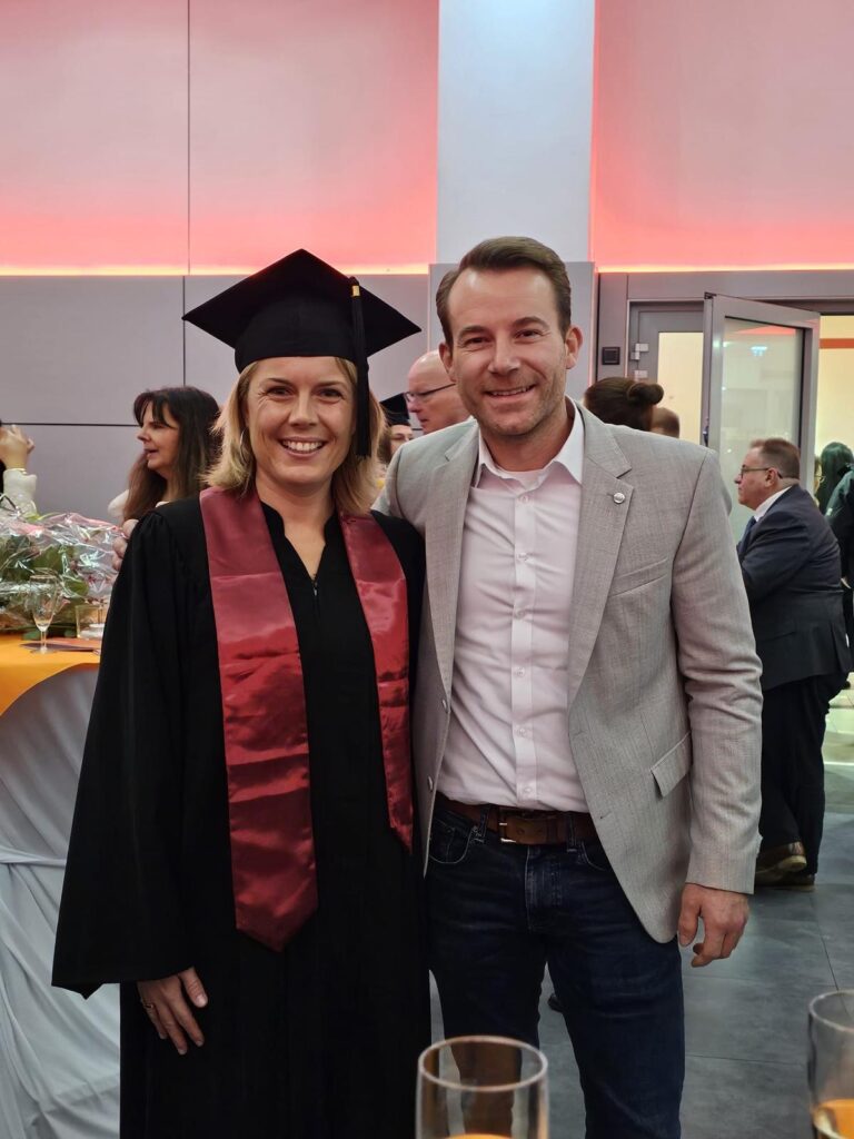 Frau Gries in akademischer Abschlussrobe mit Hut, neben Zahnarzt Dr. med. dent. Benjamin Schulte, dem Inhaber der Zahnarztpraxis 