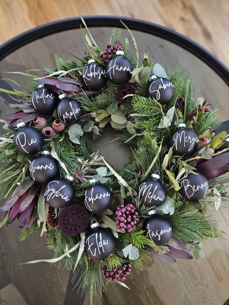 Festlicher Kranz mit mattschwarzen Kugeln und den Namen des Praxisteams als Teil der Weihnachtsdekoration der Zahnarztpraxis in Odenthal.